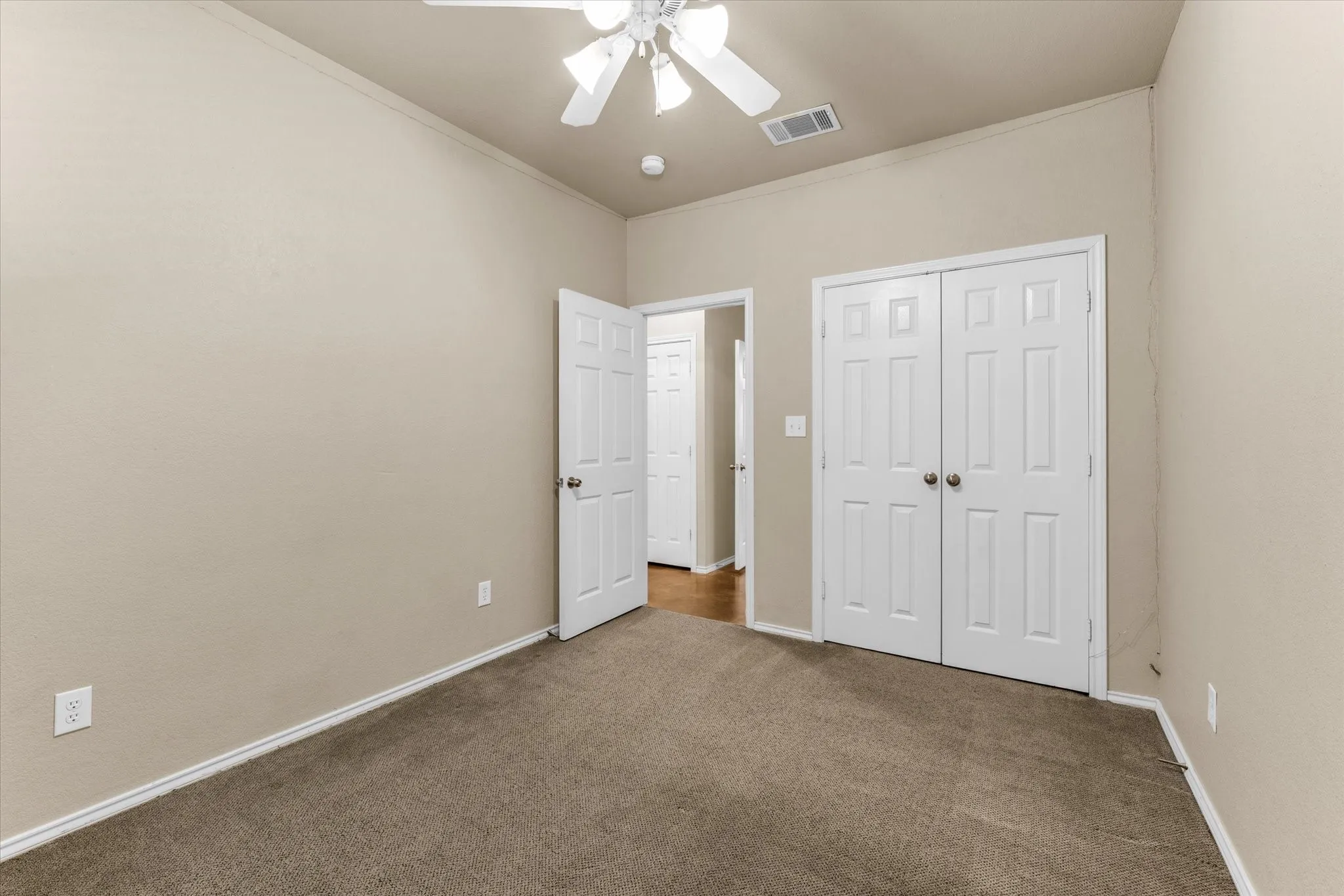 Carpeted room with neutral-toned walls, featuring a white ceiling fan with light fixture, a double-door closet, and a paneled interior door