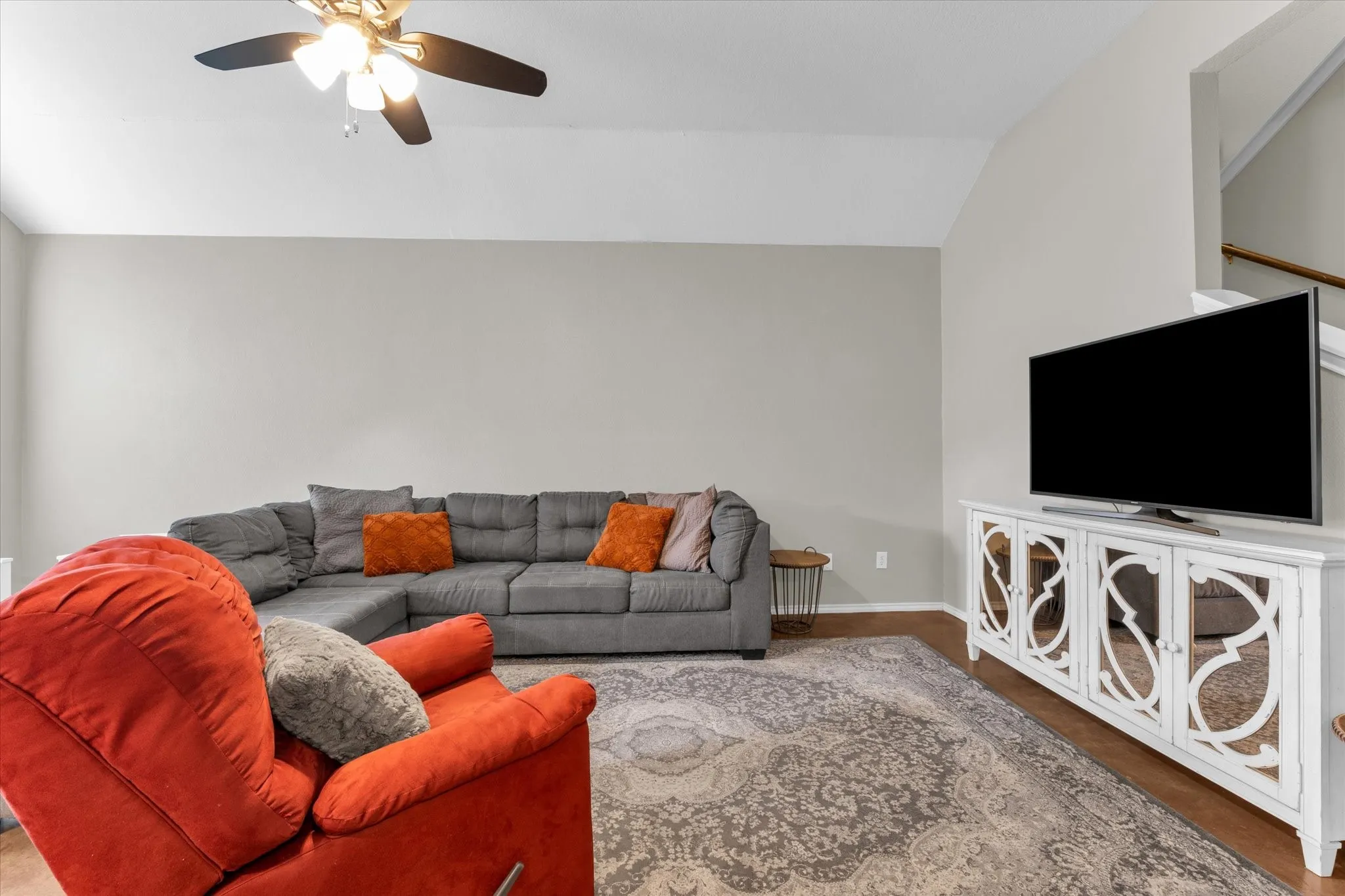 Living area featuring an angled ceiling, ceiling fan with integrated lighting, wood-finish flooring, and a decorative media console