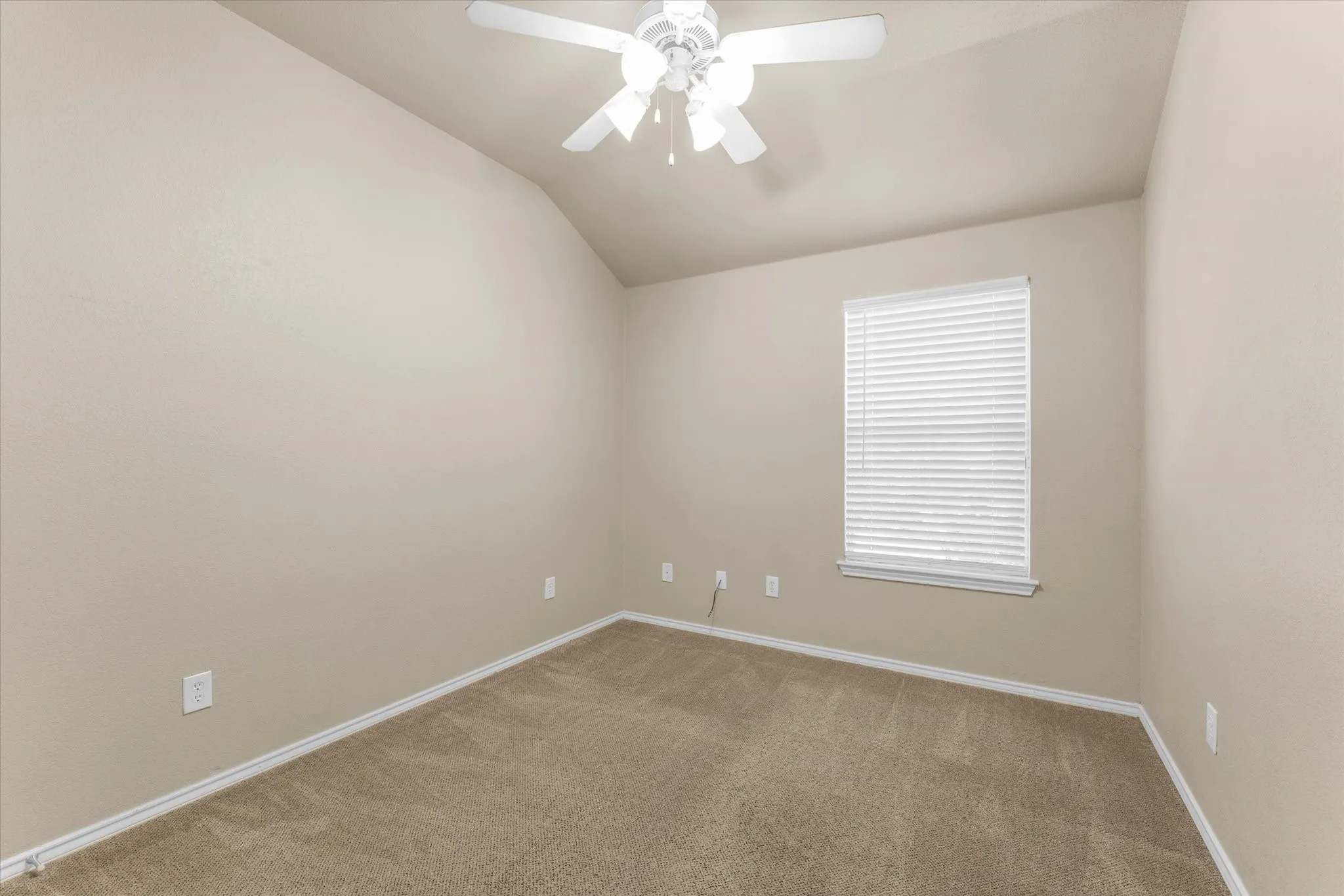 Carpeted room featuring a vaulted ceiling with a ceiling fan, a window with horizontal blinds, and neutral-toned walls