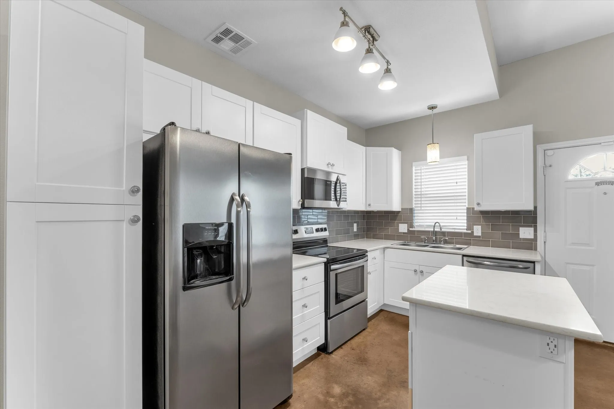 Contemporary kitchen featuring white cabinetry, stainless steel appliances, a grey subway tile backsplash, light countertops, and track lighting