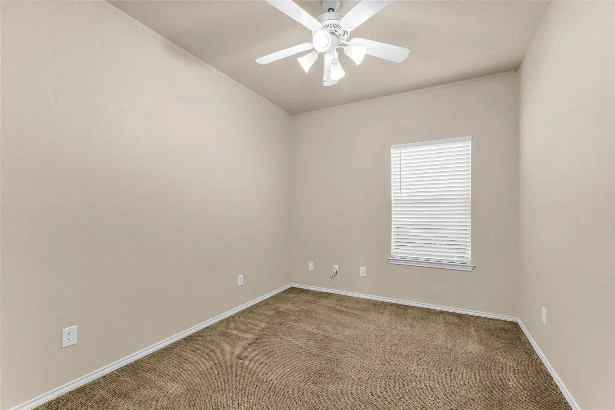 Carpeted room featuring a white ceiling fan with integrated lighting, neutral wall paint, and a window with blinds