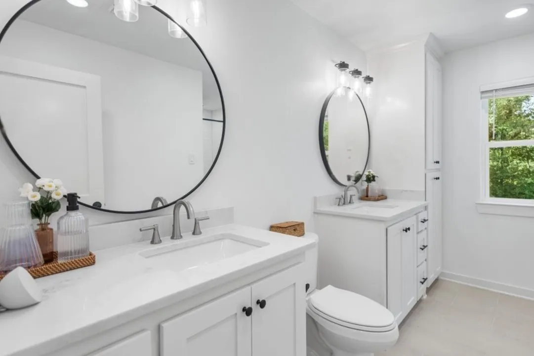 Dual vanity in Primary En Suite bathroom featuring white cabinetry, stone-finish countertops, undermount sinks, and matte black round mirrors