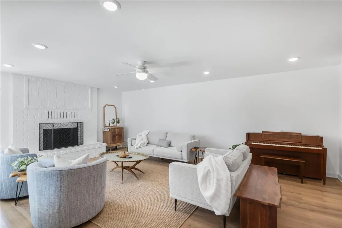 Living area featuring wood-finish flooring, a white brick fireplace, recessed lighting, and a ceiling fan