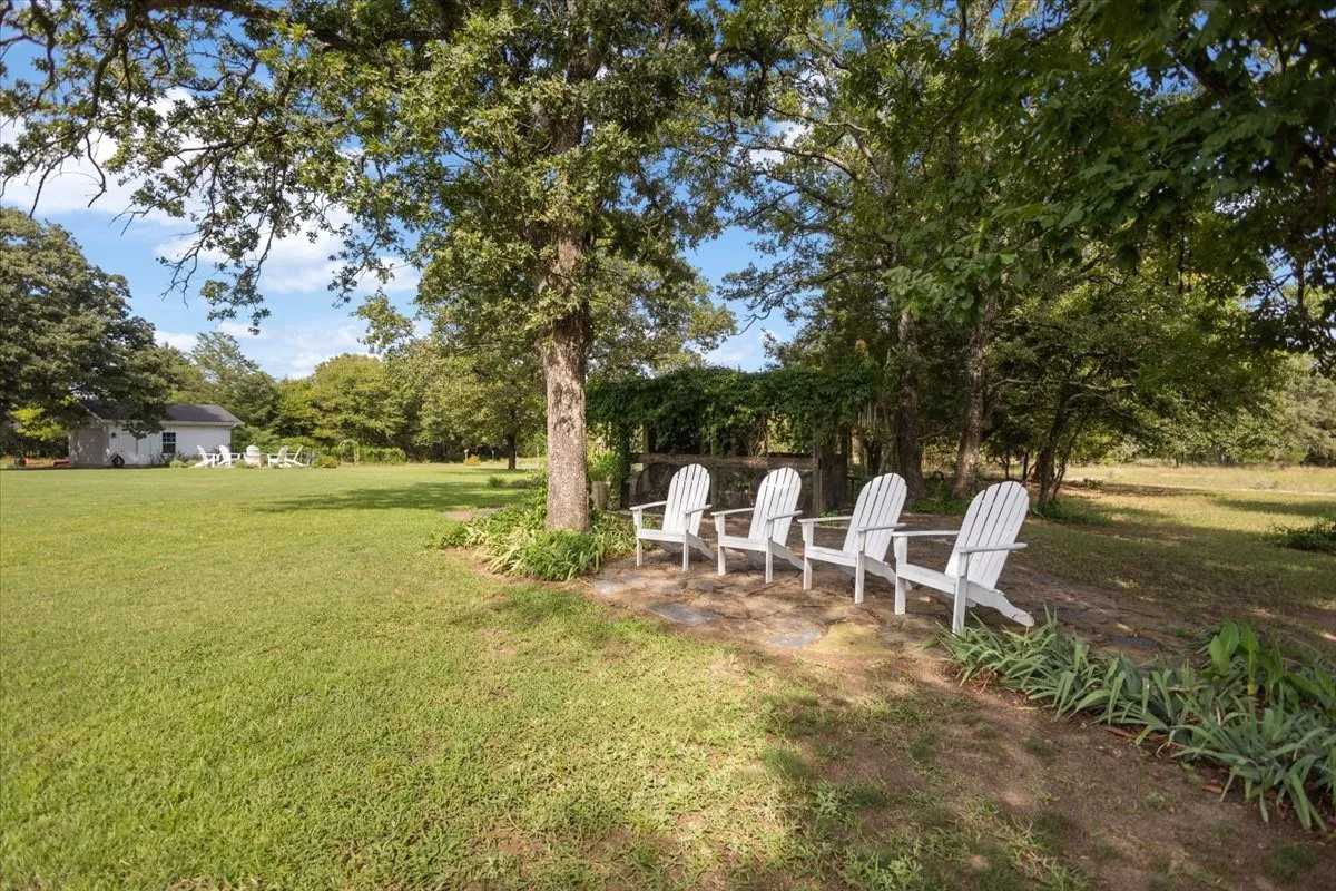 Expansive grounds featuring a manicured lawn shaded by mature trees, with Adirondack seating positioned beneath towering oaks