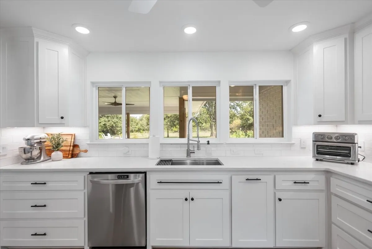Contemporary white kitchen featuring shaker-style cabinetry, a stainless steel dishwasher, a single-basin undermount sink with a gooseneck faucet, white subway tile backsplash, and recessed lighting