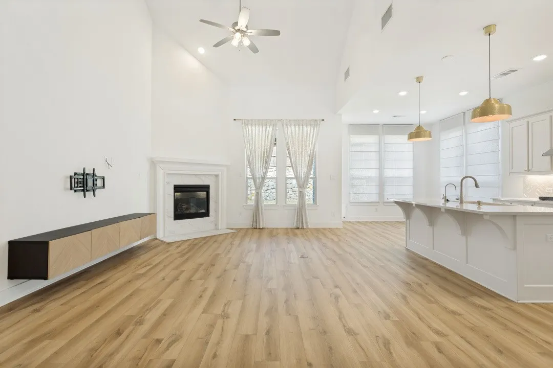 High vaulted ceiling, wood-finish flooring, white stone fireplace, and a kitchen island with pendant lighting