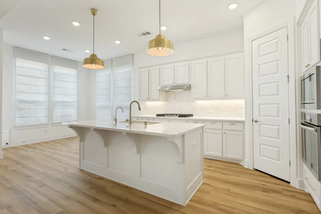 Kitchen featuring an expansive island with dual sinks, overhead pendant lighting, white cabinetry, integrated stainless steel appliances, and wood-finish flooring