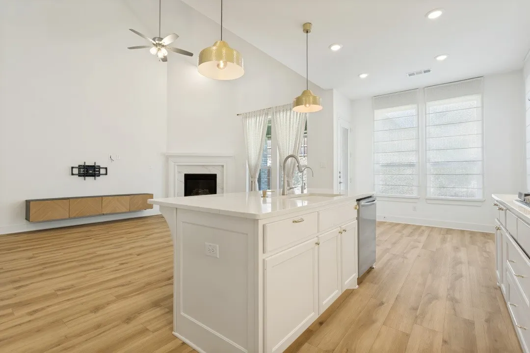 Vaulted ceilings with ceiling fan, white kitchen island with countertop, stainless steel sink with gooseneck faucet, two pendant light fixtures, and wood-finish flooring