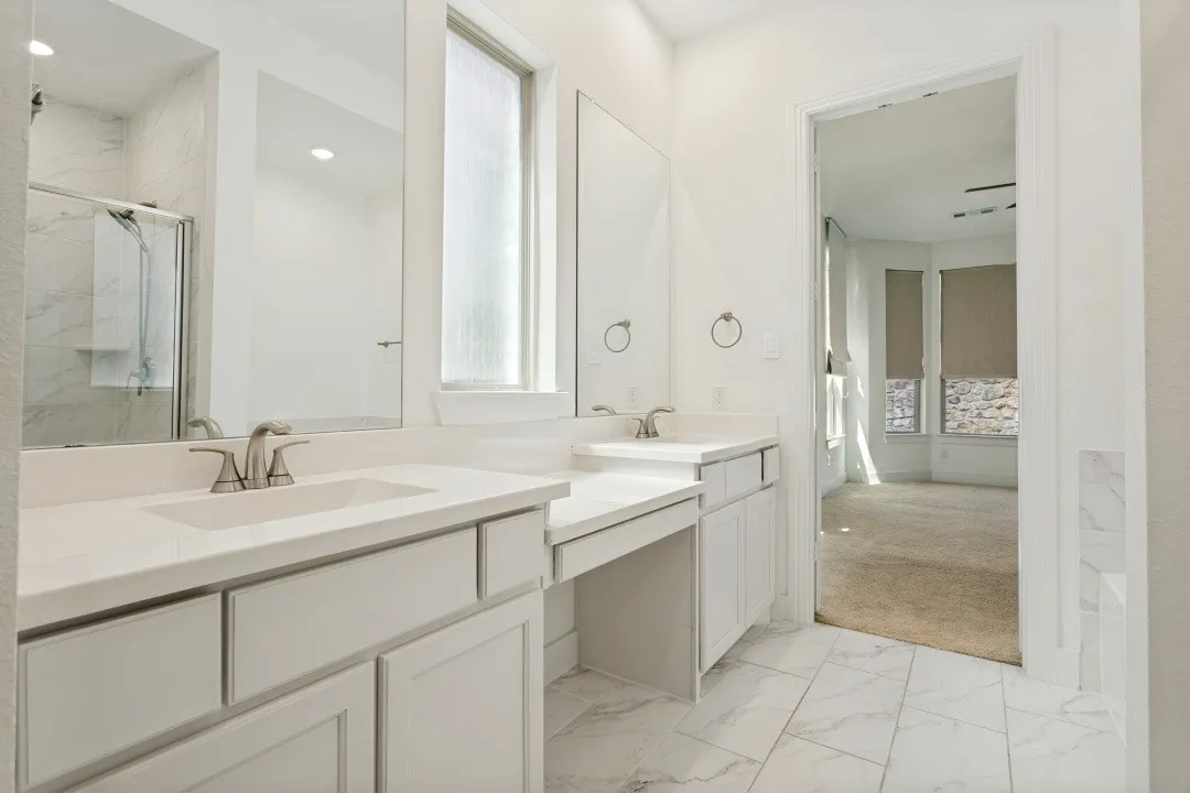 Spa-inspired primary bathroom featuring dual vanities with white cabinetry, white quartz countertops, and brushed nickel faucet fixtures
