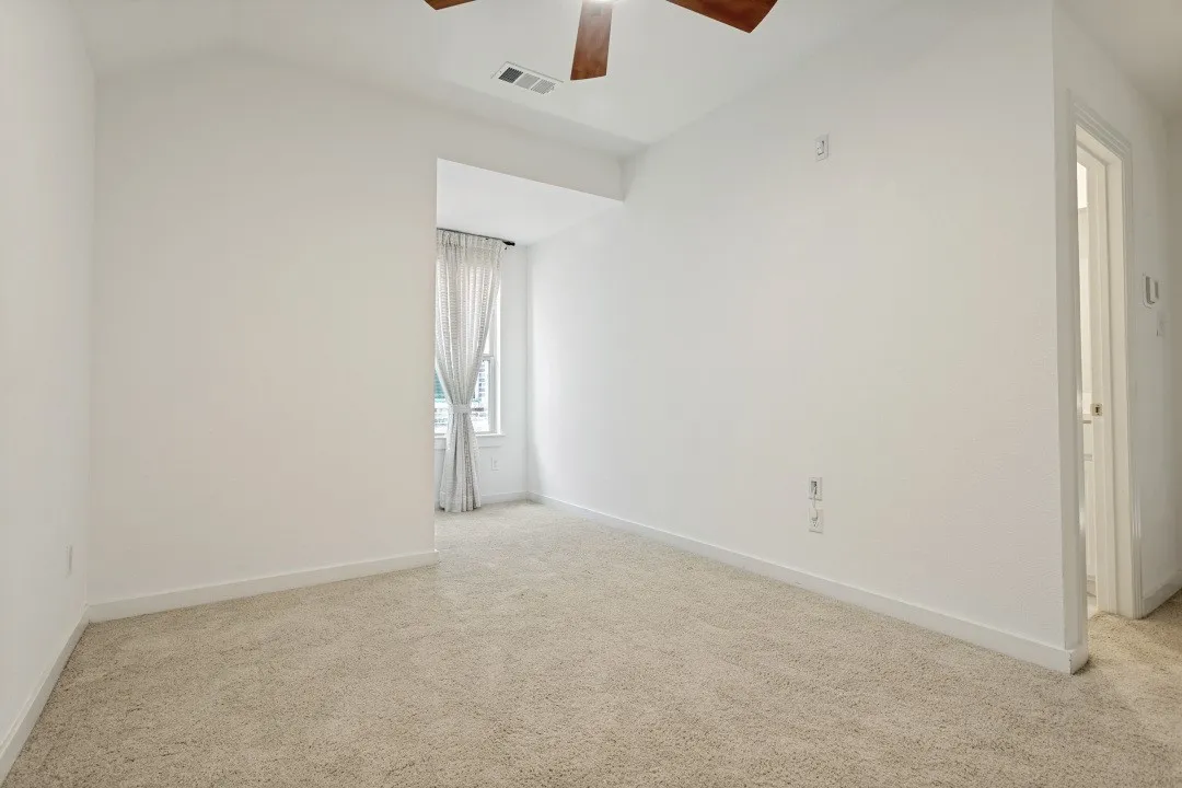 Neutral-toned carpeting, white painted walls, and a window with sheer curtains