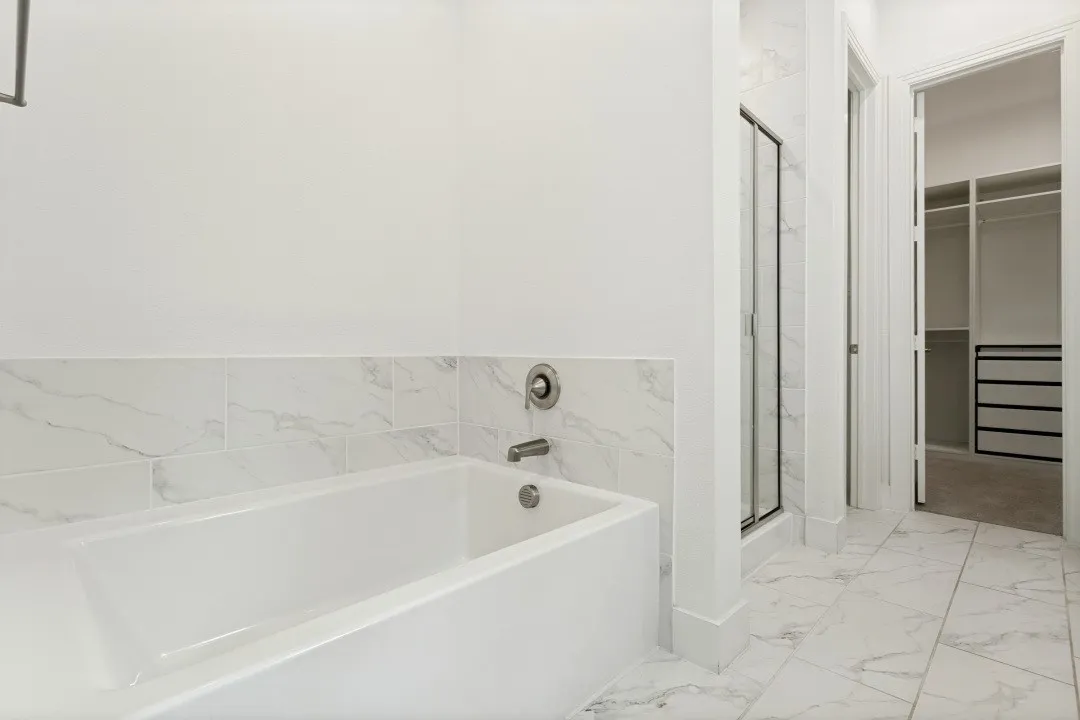 Soaking tub with chrome fixtures, tiled shower with glass enclosure, white marble-look floor tiles, and custom closet system