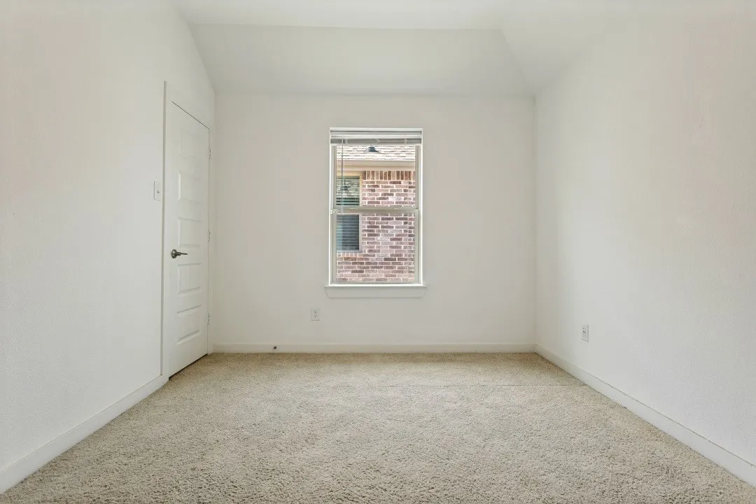 Carpeted flooring, white walls, single window with blinds, and a white interior door