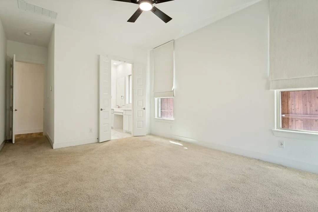 Spacious room featuring vaulted ceilings, carpet flooring, a ceiling fan, and double doors opening to a bathroom with a dual vanity