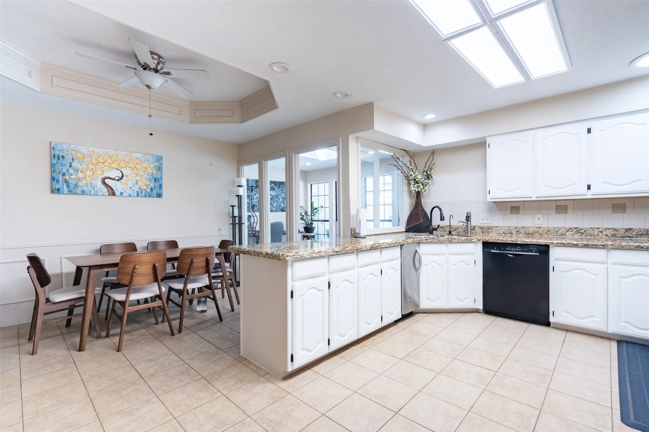 Open-concept kitchen and dining area featuring white cabinetry, granite countertops, tile flooring, and a multi-light ceiling fan