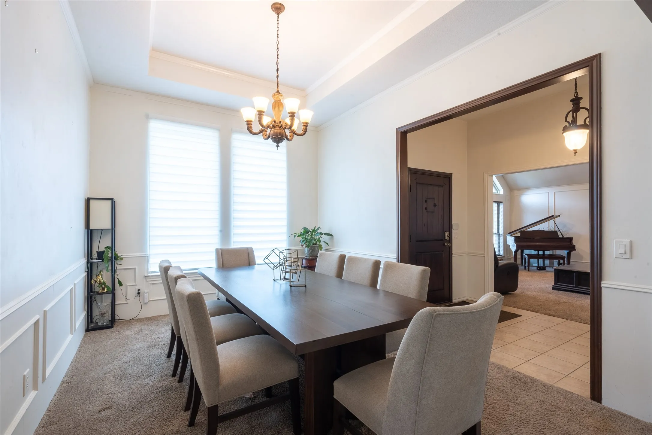 Formal dining area featuring a tray ceiling with a chandelier, wainscoting, and large windows with blinds