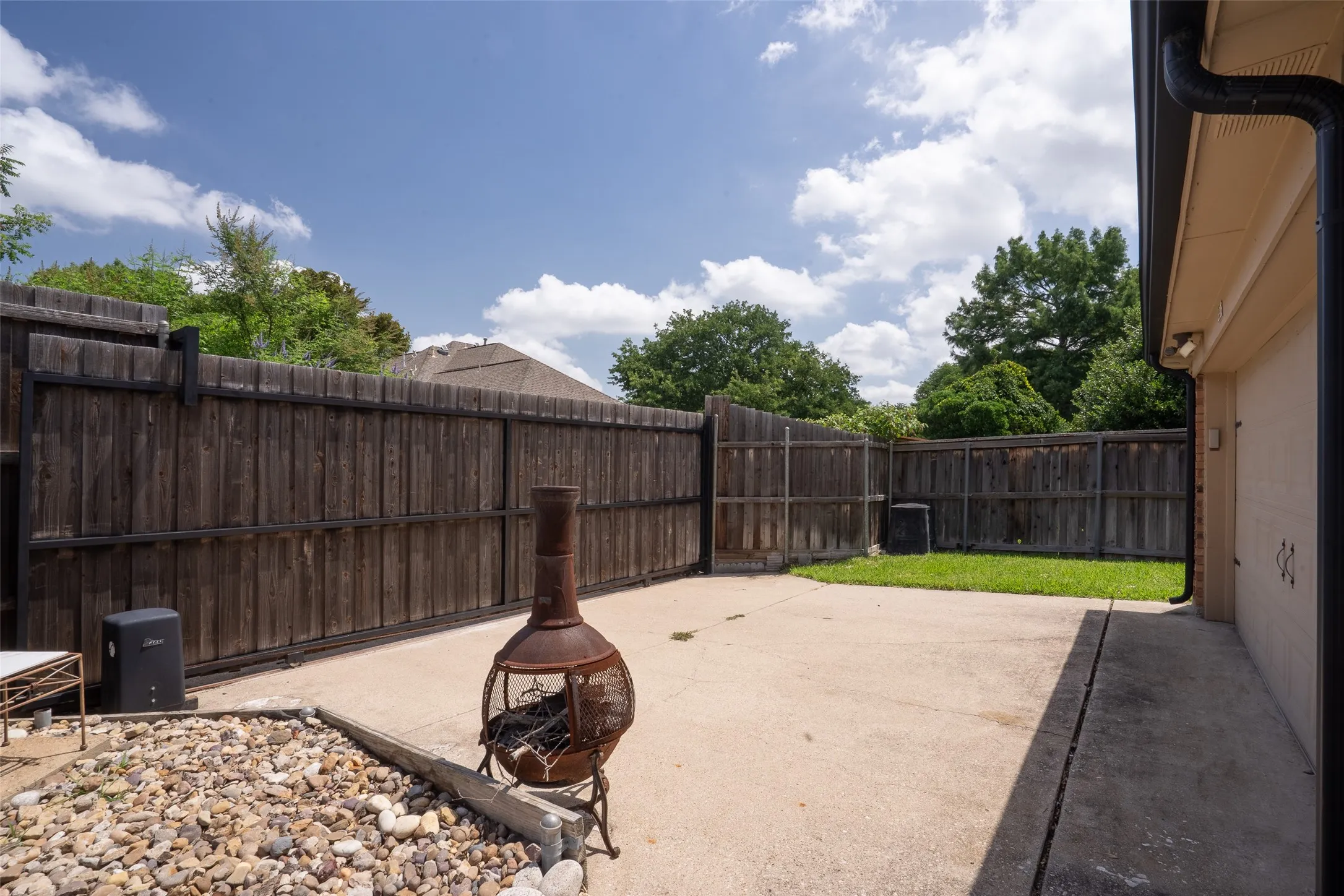 Spacious backyard featuring a full perimeter privacy fence, concrete patio, and a dedicated gravel area