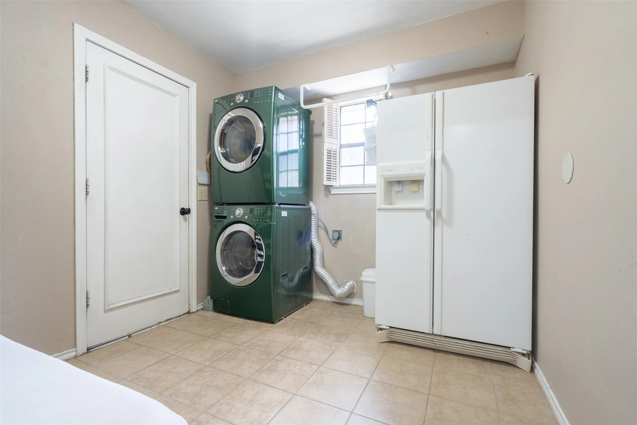 Utility area featuring a side-by-side refrigerator with water and ice dispenser, window with shutters, tan tile flooring, and light-colored walls