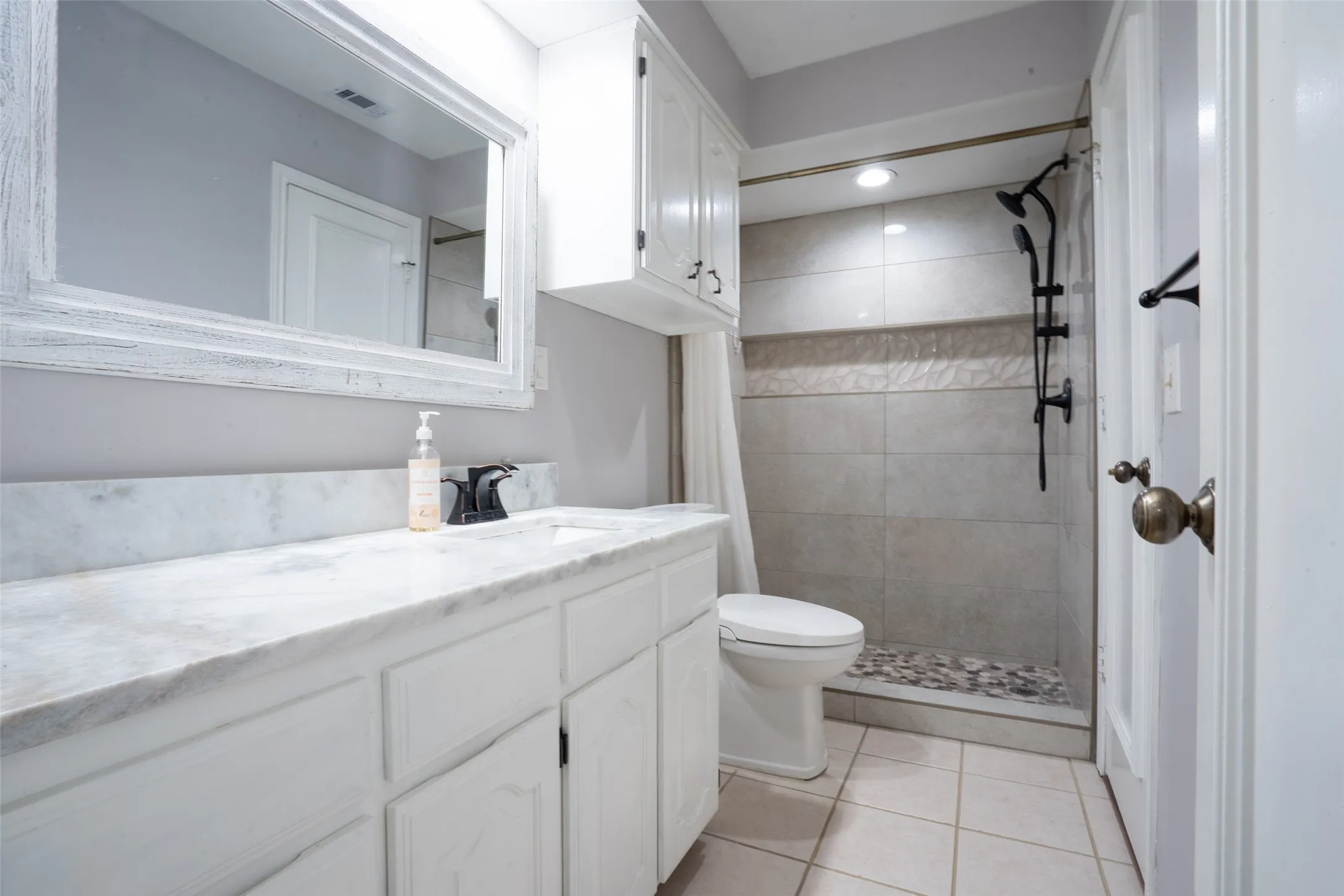 Bathroom featuring a white vanity with a light-toned countertop, a shower with tiled walls and a pebble-stone floor, and a wall-mounted medicine cabinet