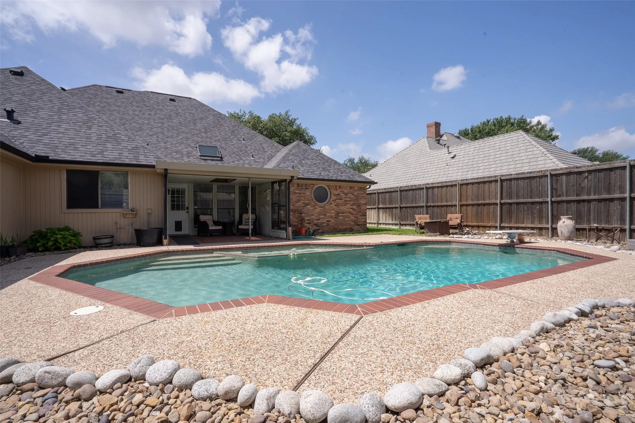 Backyard featuring an in-ground pool with stone coping and a concrete surround