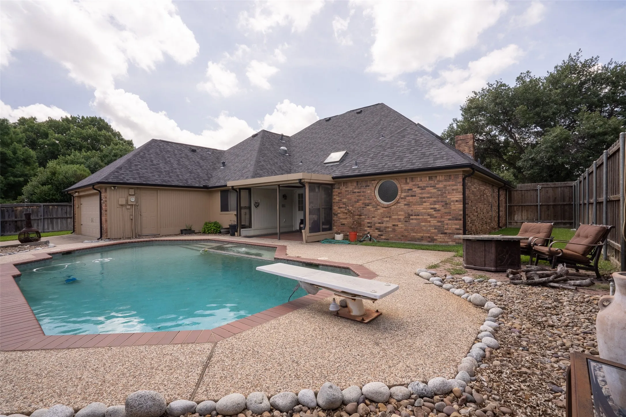 Expansive backyard featuring a built-in swimming pool with a diving board, surrounding exposed aggregate patio, and a covered patio area