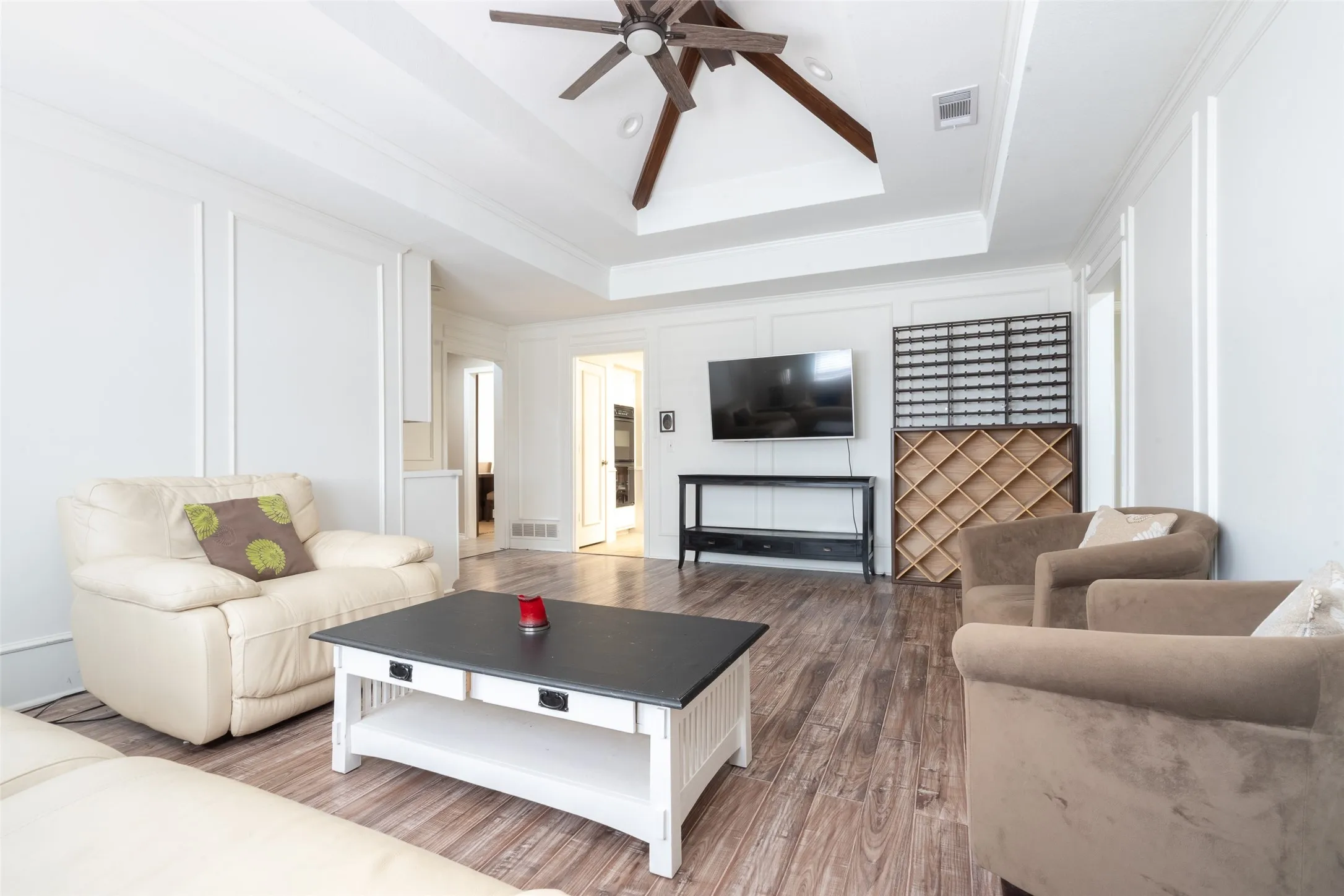Living area featuring wood-finish flooring, white paneled walls, and a recessed ceiling with exposed wood beams