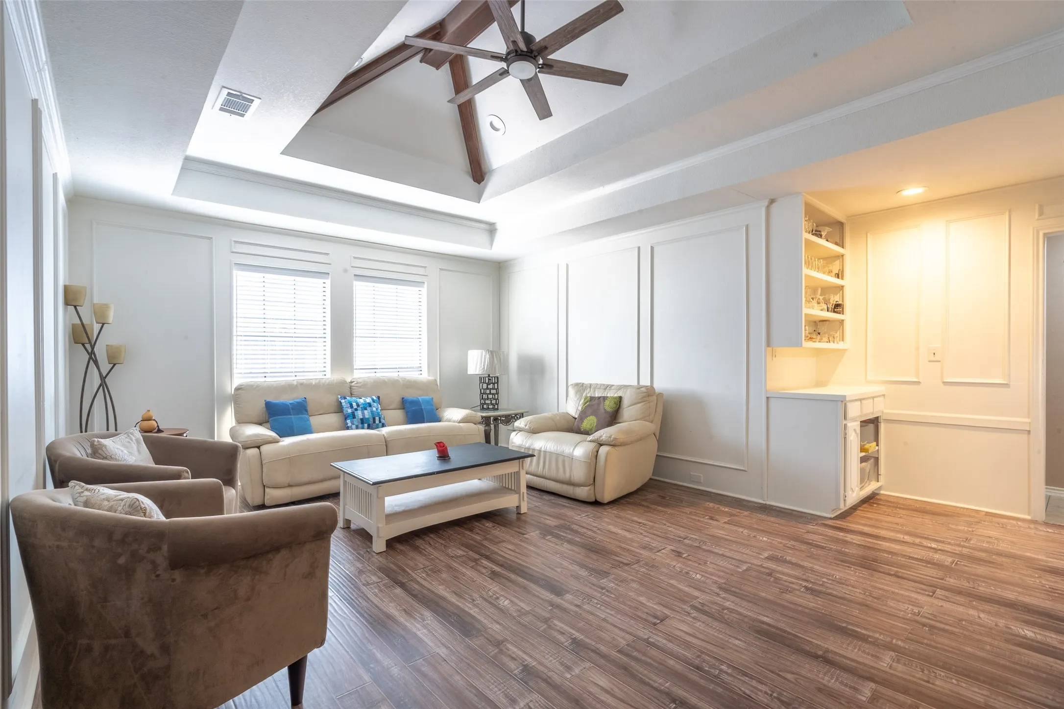 Spacious living area featuring wood-finish flooring and a tray ceiling with a ceiling fan