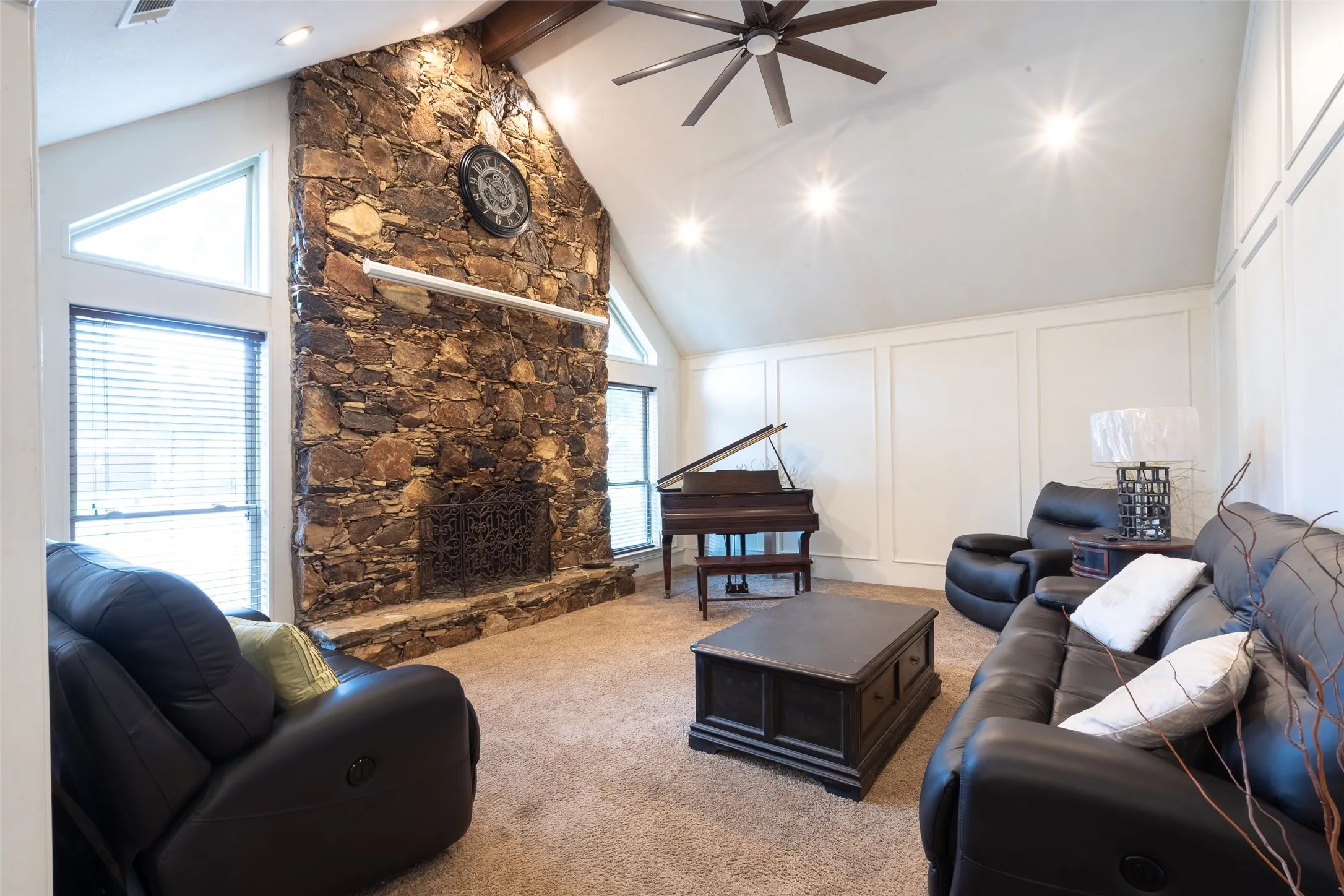 Spacious living area featuring a vaulted ceiling with exposed wood beam, recessed lighting, and a prominent floor-to-ceiling stone fireplace