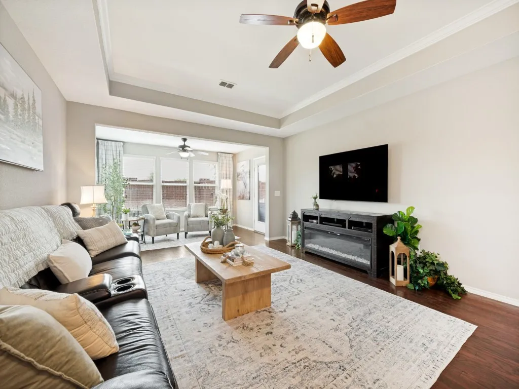 Spacious living area featuring wood-finish flooring, a tray ceiling with crown molding, and a built-in entertainment console