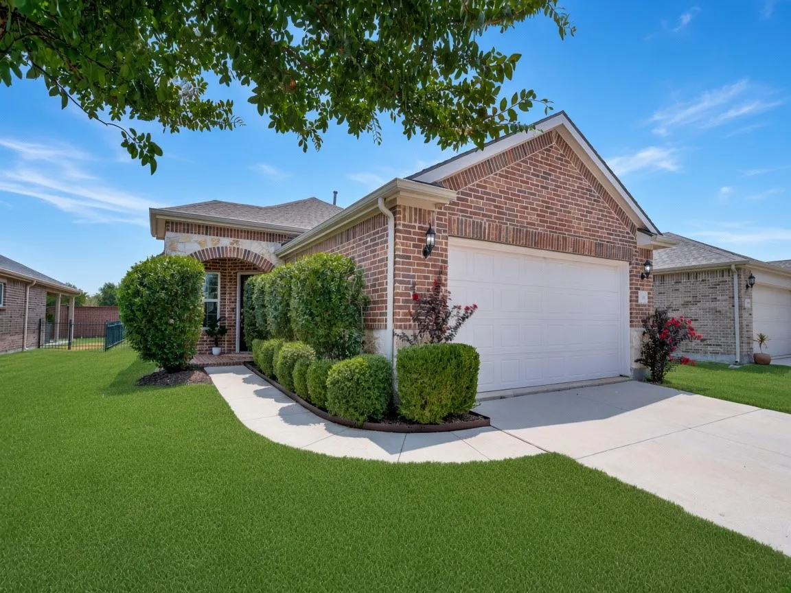 Brick exterior featuring stone accents and a two-car garage.  Grass has been digitally enhanced.