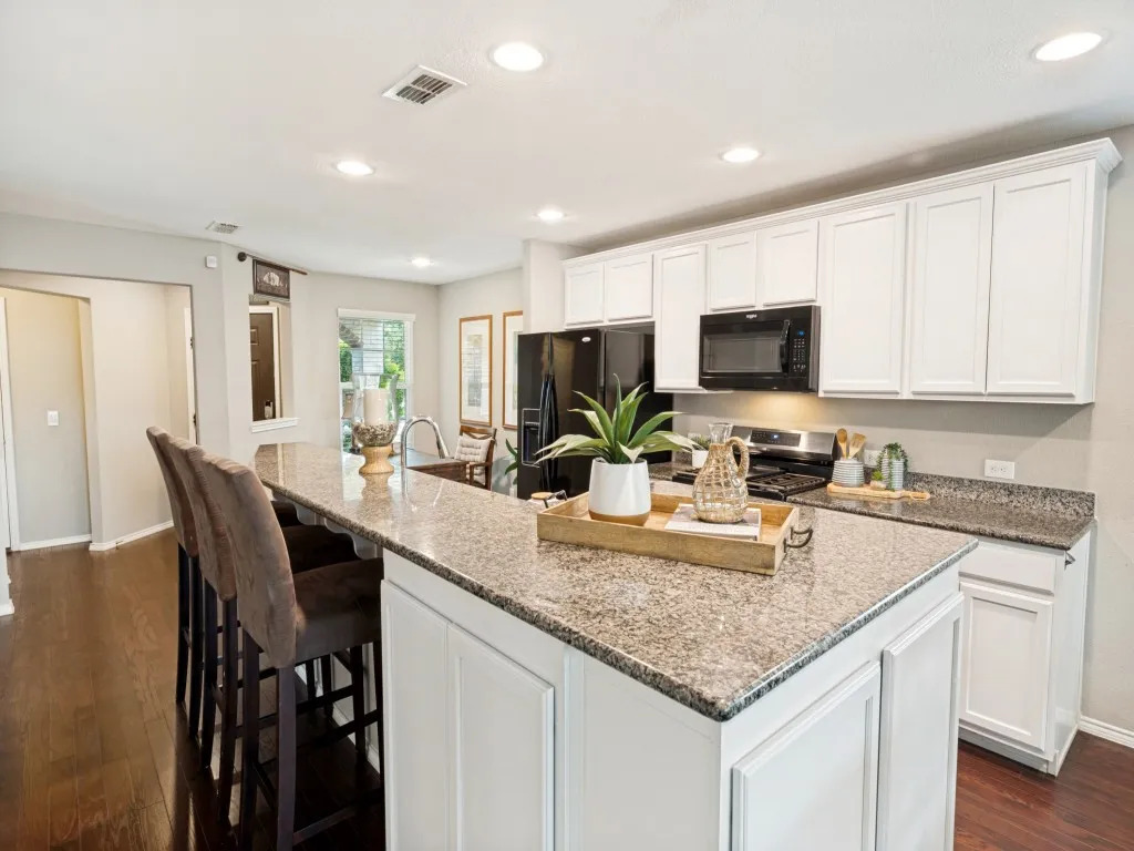 Kitchen featuring a spacious island with granite countertops, white cabinetry, dark wood-finish flooring, recessed lighting, and black appliances