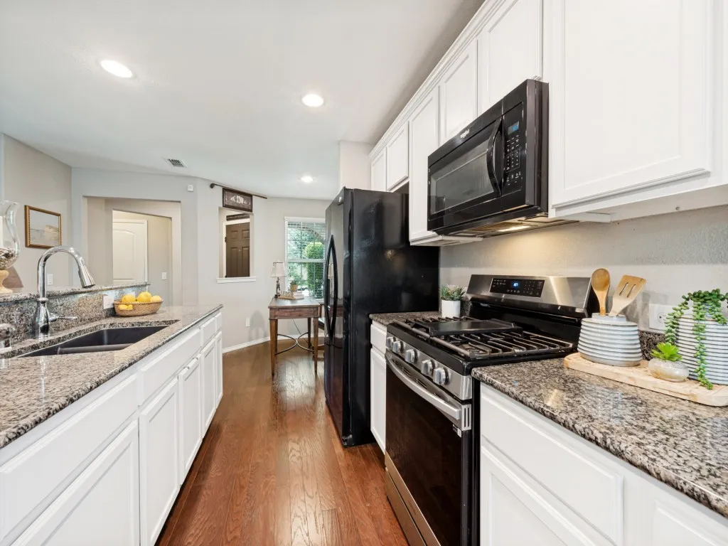 Kitchen featuring granite countertops, a double basin sink with a high-arc faucet, white cabinetry, a gas range, and wood-finish flooring