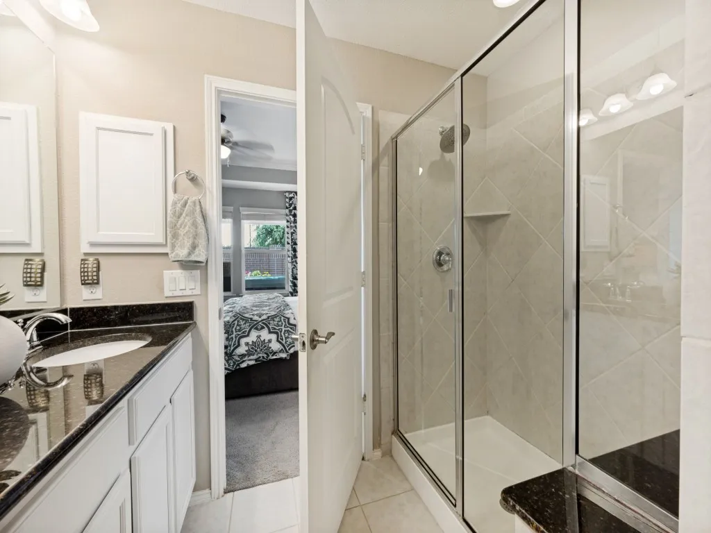 Bathroom featuring a glass-enclosed shower with tile surround, a built-in shower bench, and a vanity with a dark countertop and undermount sink