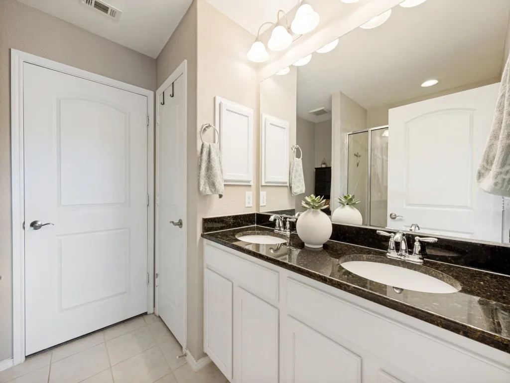 Bathroom with dual vanity featuring a dark stone countertop, undermount sinks, and chrome fixtures