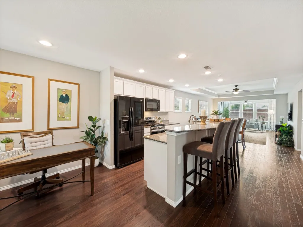 Open-concept kitchen and living area featuring dark wood-finish flooring, a kitchen island with seating, recessed lighting, and white cabinets