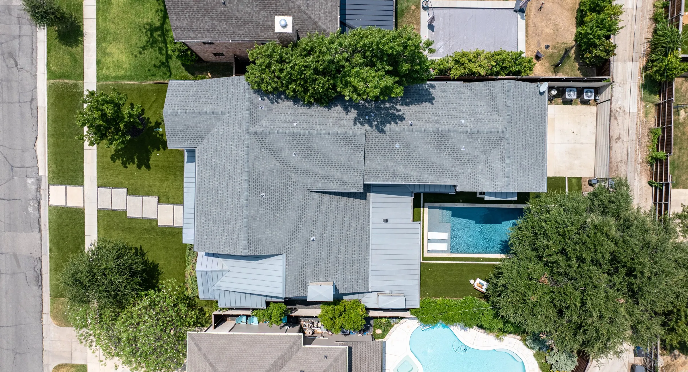 Expansive property featuring a grey shingle roof, a rectangular swimming pool with integrated tanning ledge, and a manicured lawn