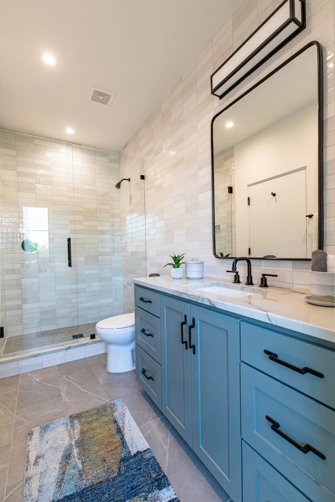 Bathroom featuring a light blue vanity with black hardware, a rectangular mirror, and a glass-enclosed shower with black fixtures