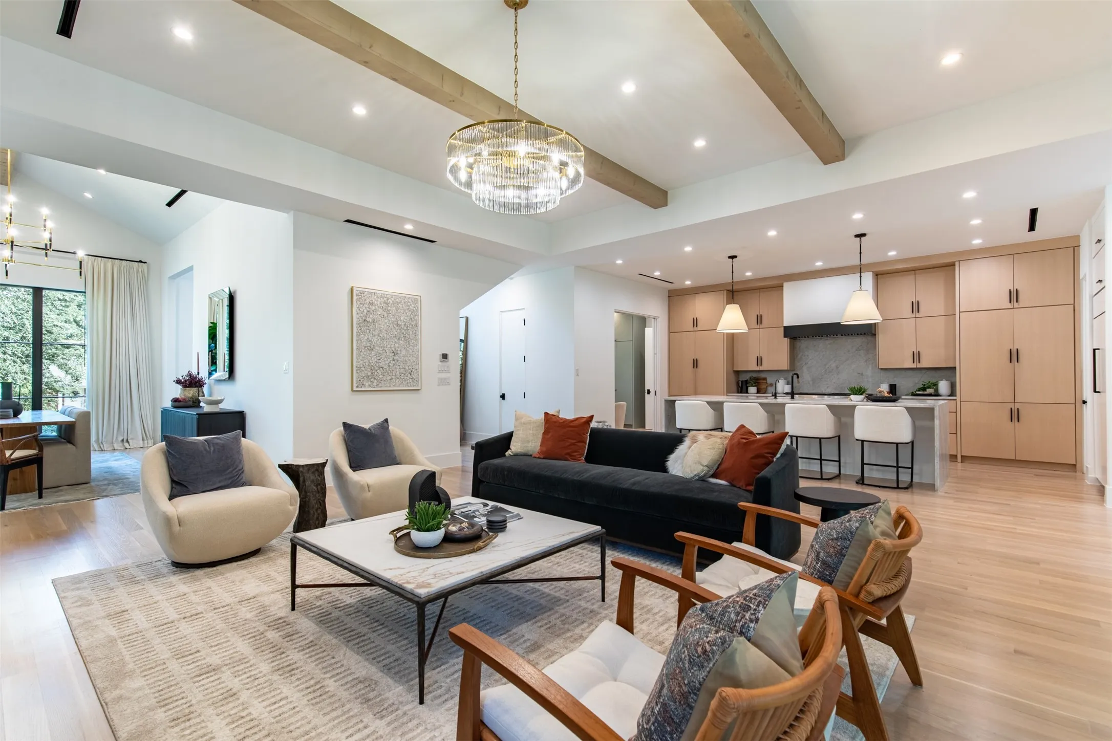 Open-concept living area featuring light wood-finish flooring, exposed ceiling beams, and a contemporary chandelier