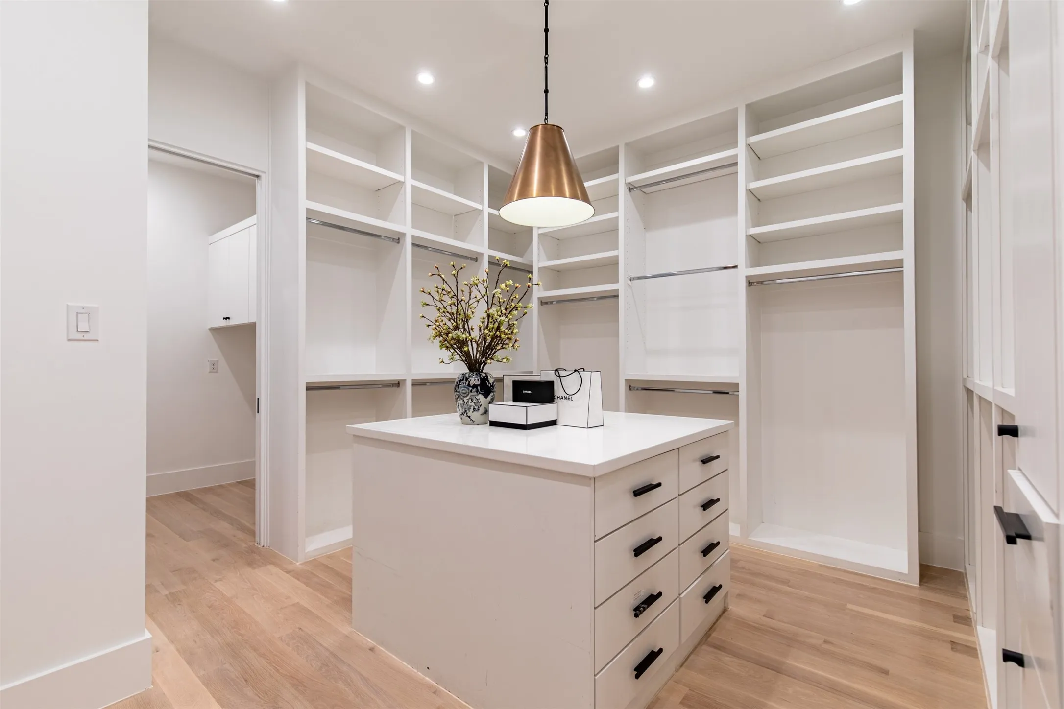 Spacious walk-in closet featuring light wood-finish flooring, recessed lighting, and a central island with integrated drawers
