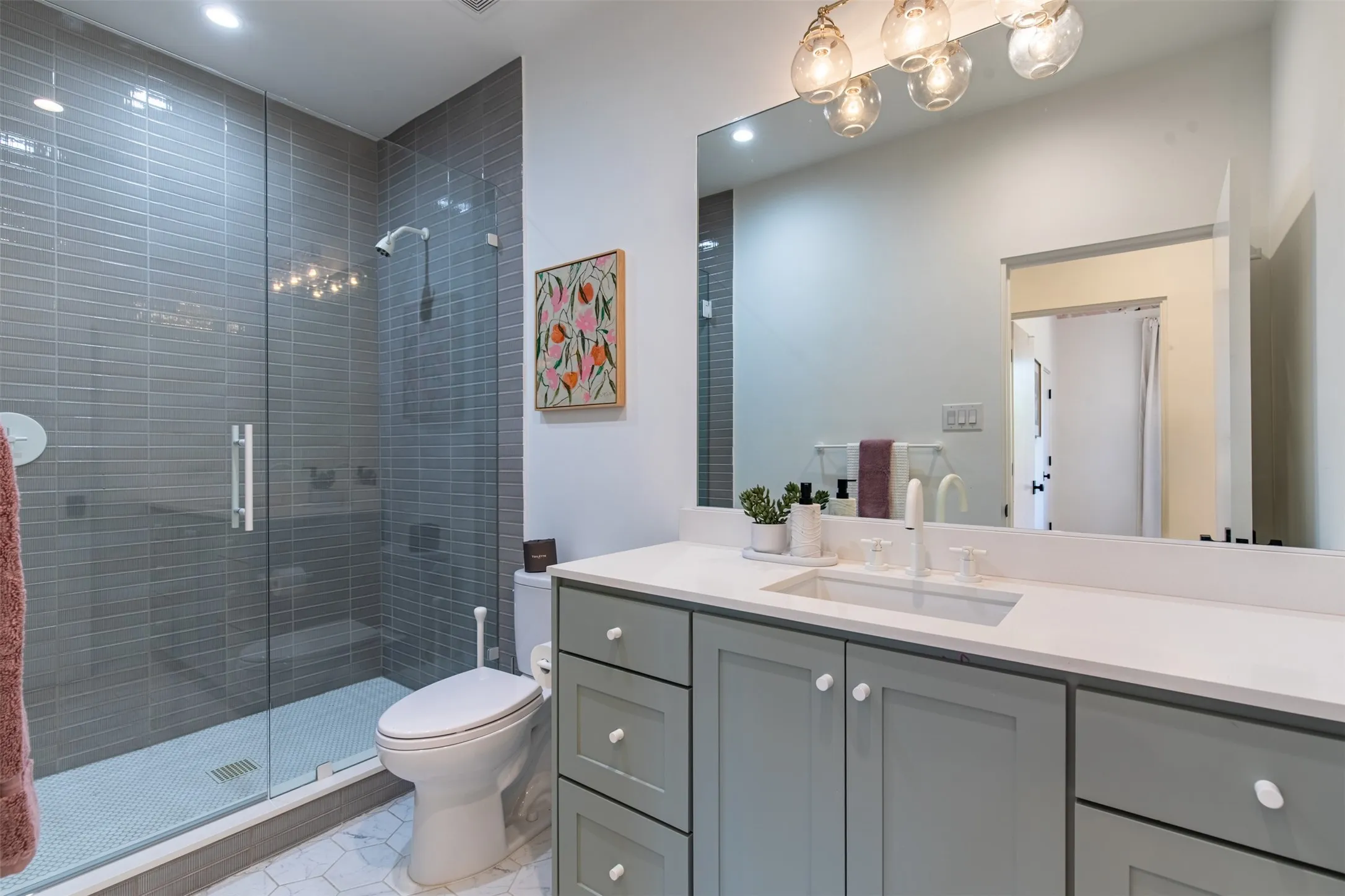 Modern bathroom featuring a glass-enclosed shower with gray subway tile surround, white hex tile flooring, and a vanity with a white countertop