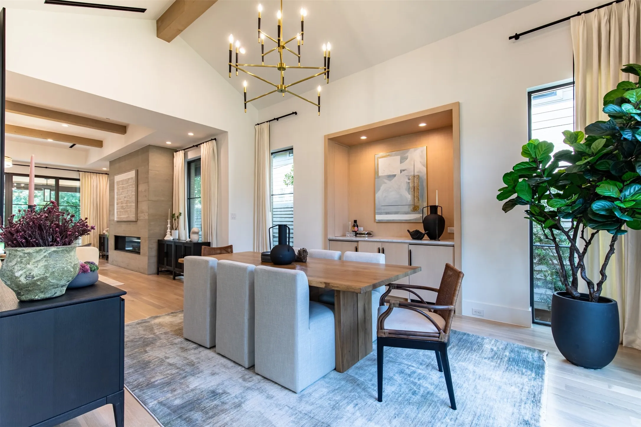 Vaulted ceiling dining area featuring a linear chandelier, wood-finish flooring, and a built-in recessed cabinet with lower storage