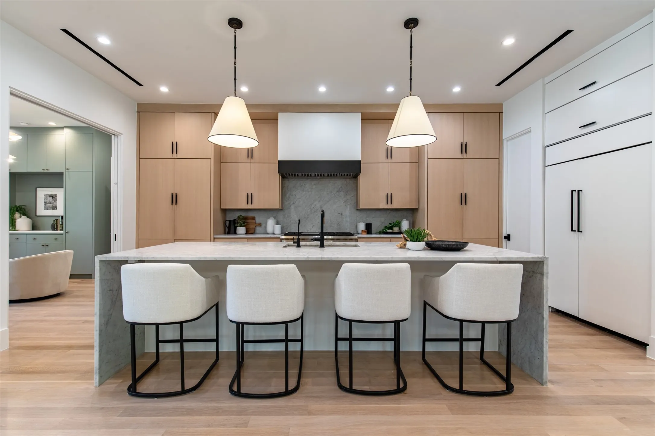 Modern kitchen featuring a large waterfall island with seating, light wood-finish cabinetry, integrated appliances, and recessed lighting