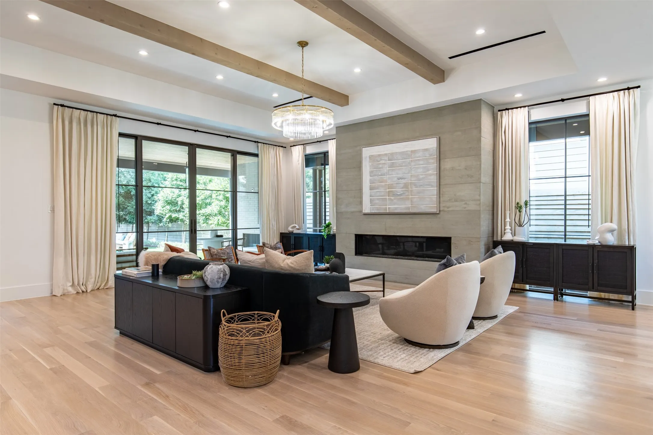 Open-concept living space featuring wood-finish flooring, a linear fireplace set into a stone-clad wall, and exposed ceiling beams