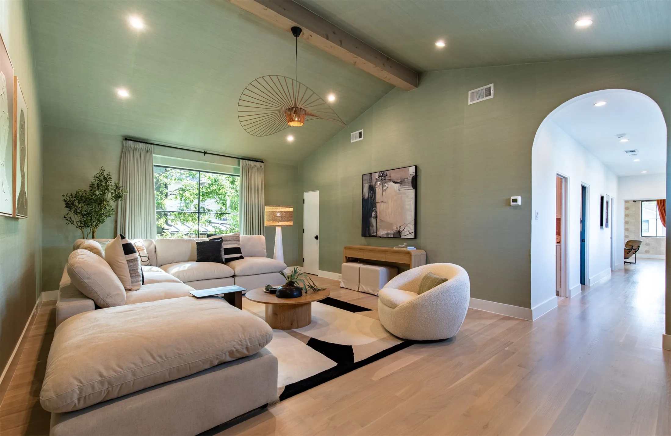 Spacious living area featuring vaulted ceilings with exposed beam, recessed lighting, and light wood-finish flooring