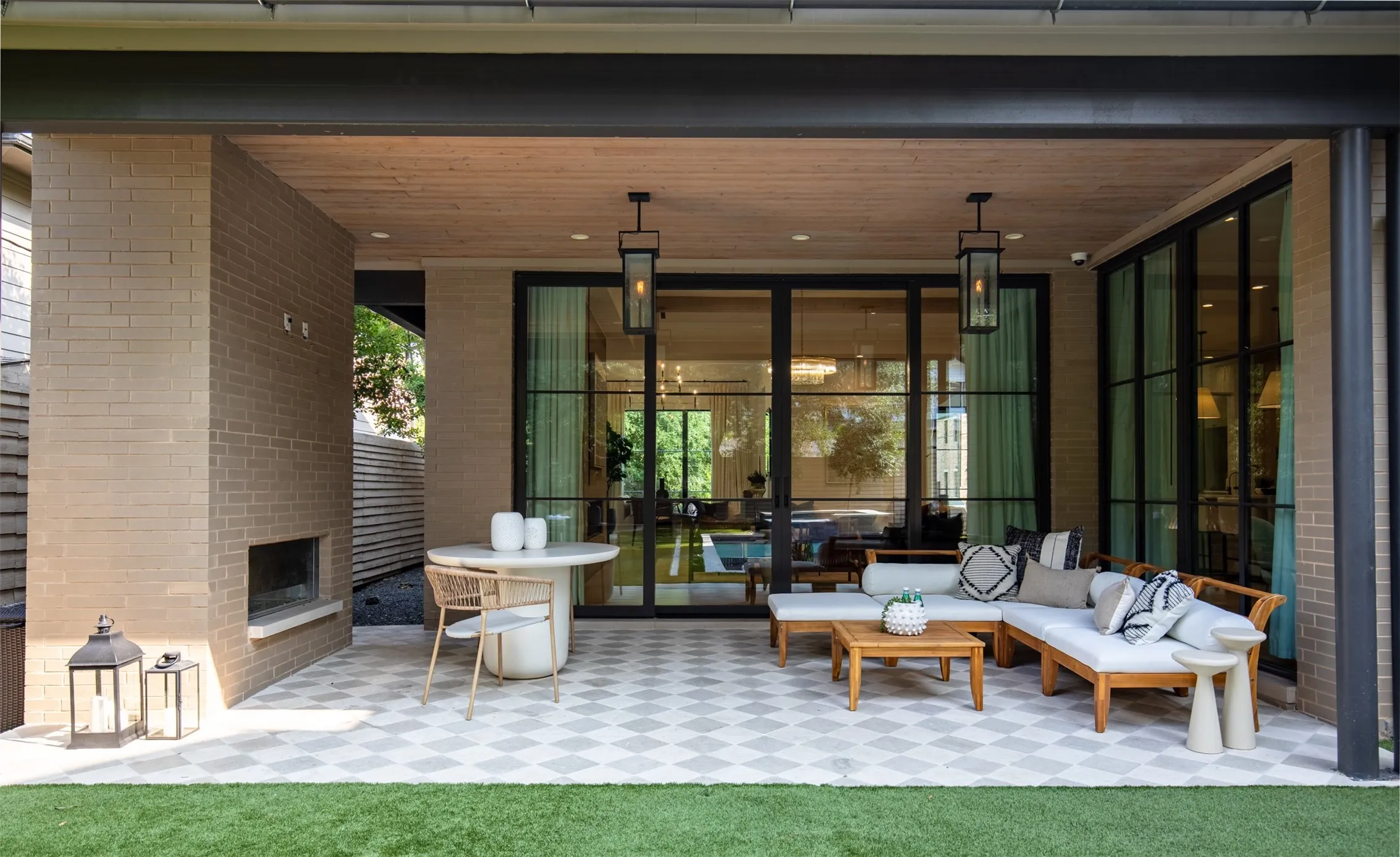 Expansive covered patio featuring a brick fireplace, geometric patterned tile flooring, and a wood-finish ceiling