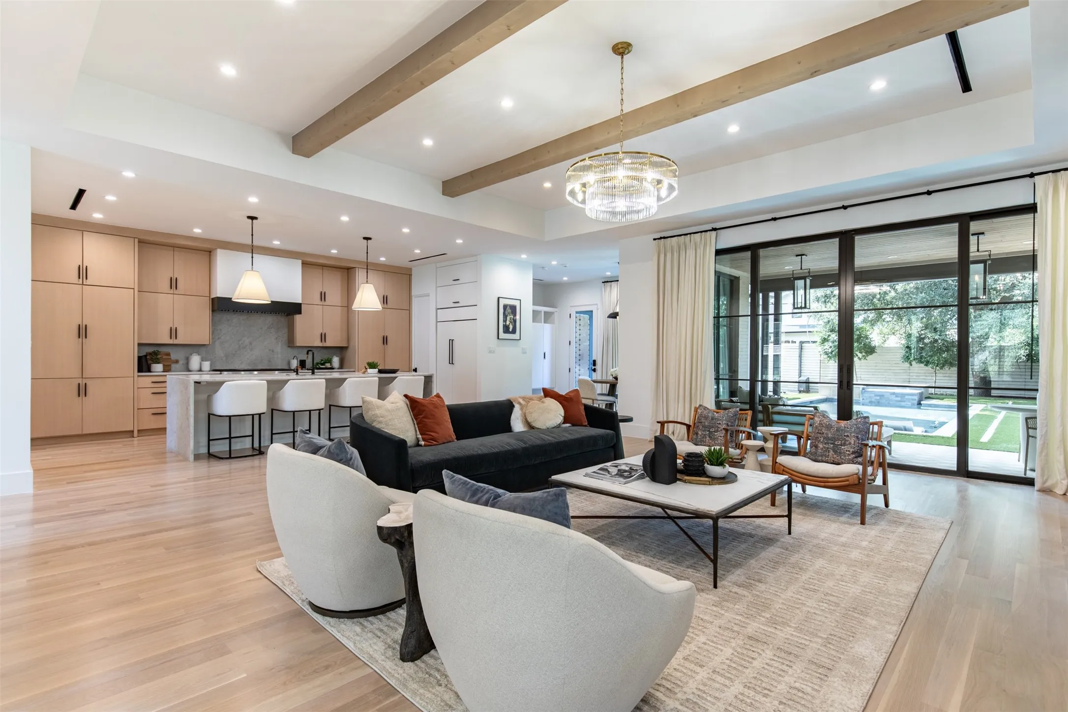 Spacious living area featuring light wood-finish flooring, exposed ceiling beams, and a contemporary chandelier