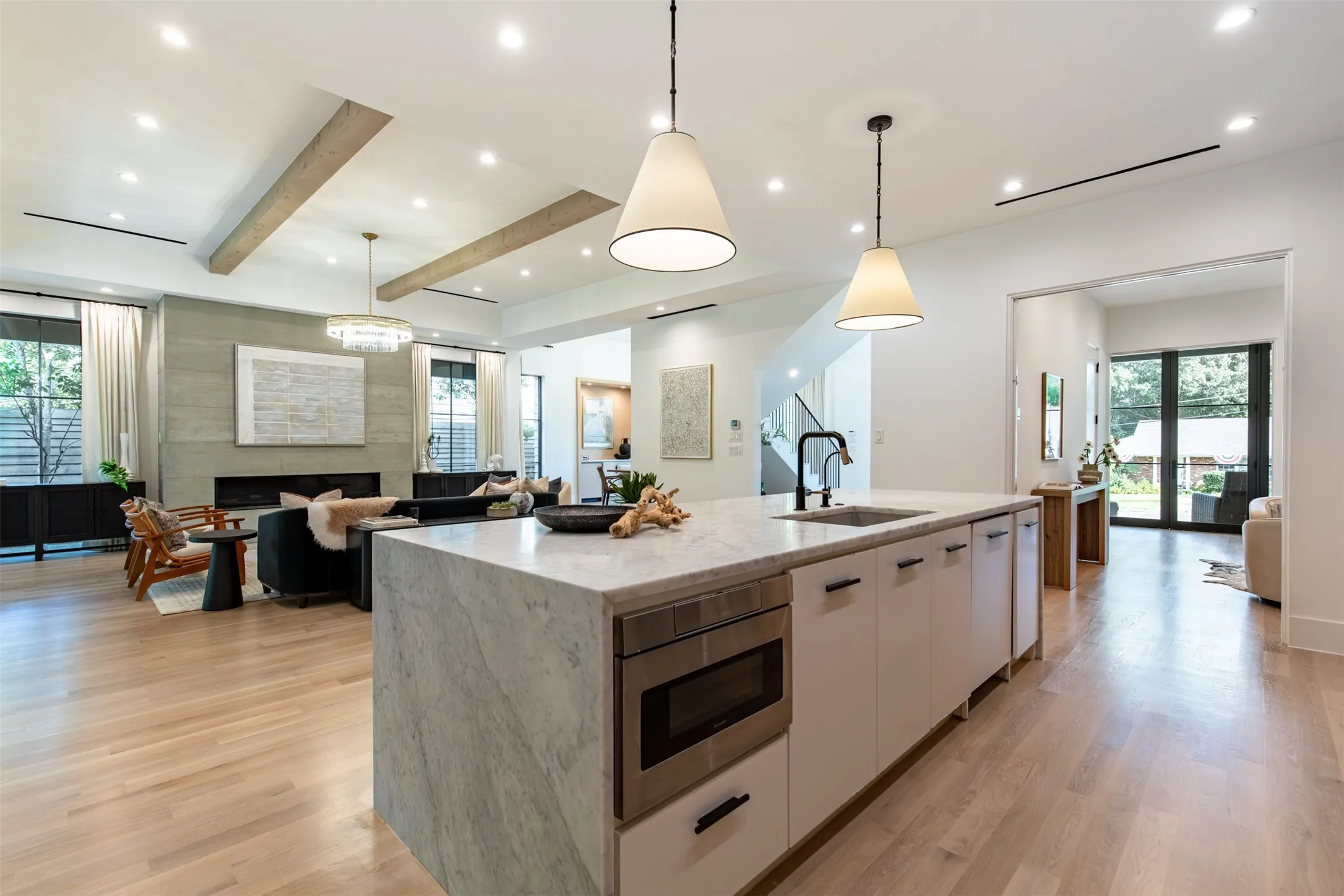 Open-concept living space featuring a waterfall island with integrated microwave, wood-finish flooring, recessed lighting, and exposed ceiling beams