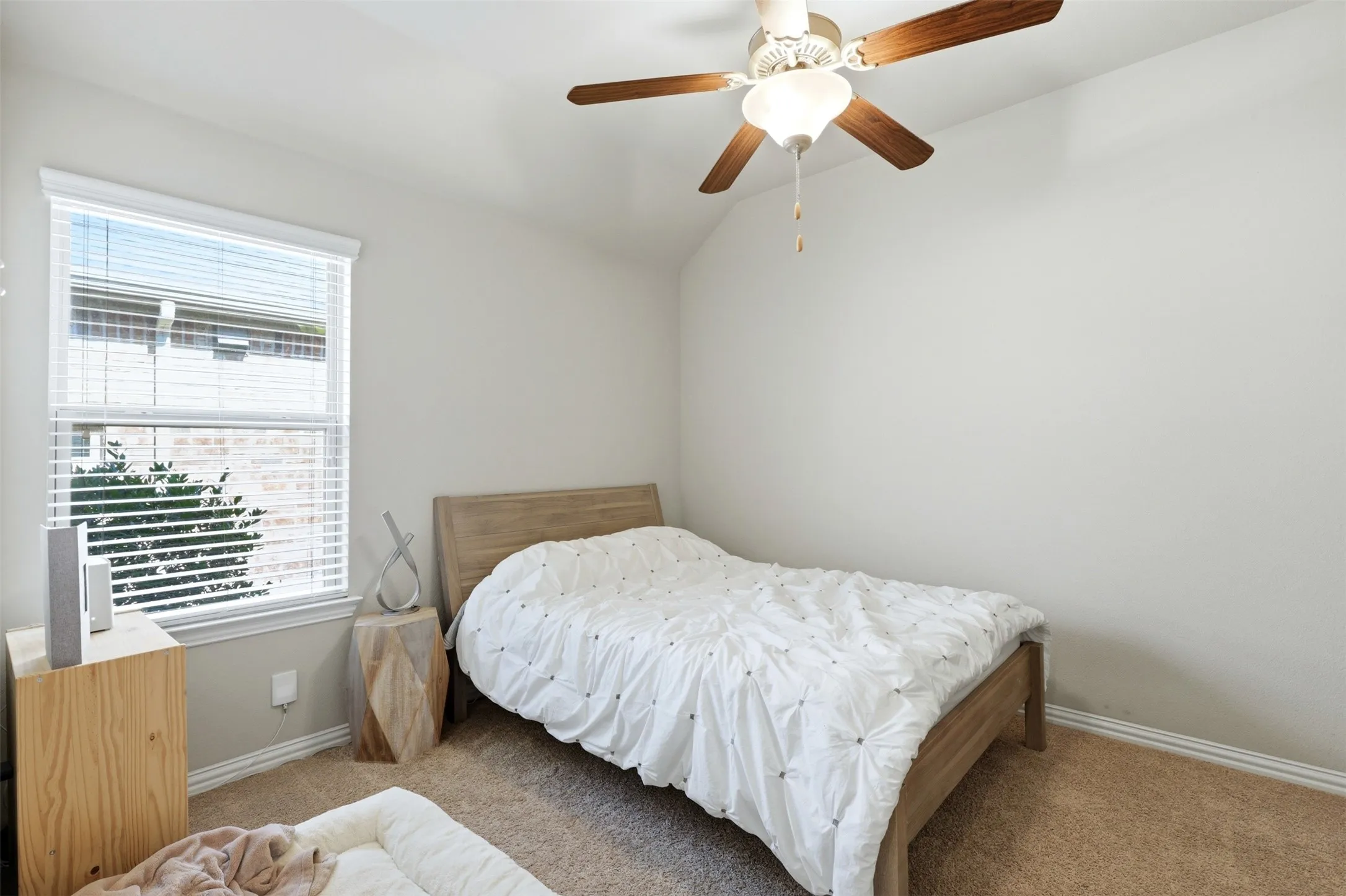 Carpeted flooring, vaulted ceiling, single window with blinds, and a ceiling fan with integrated lighting