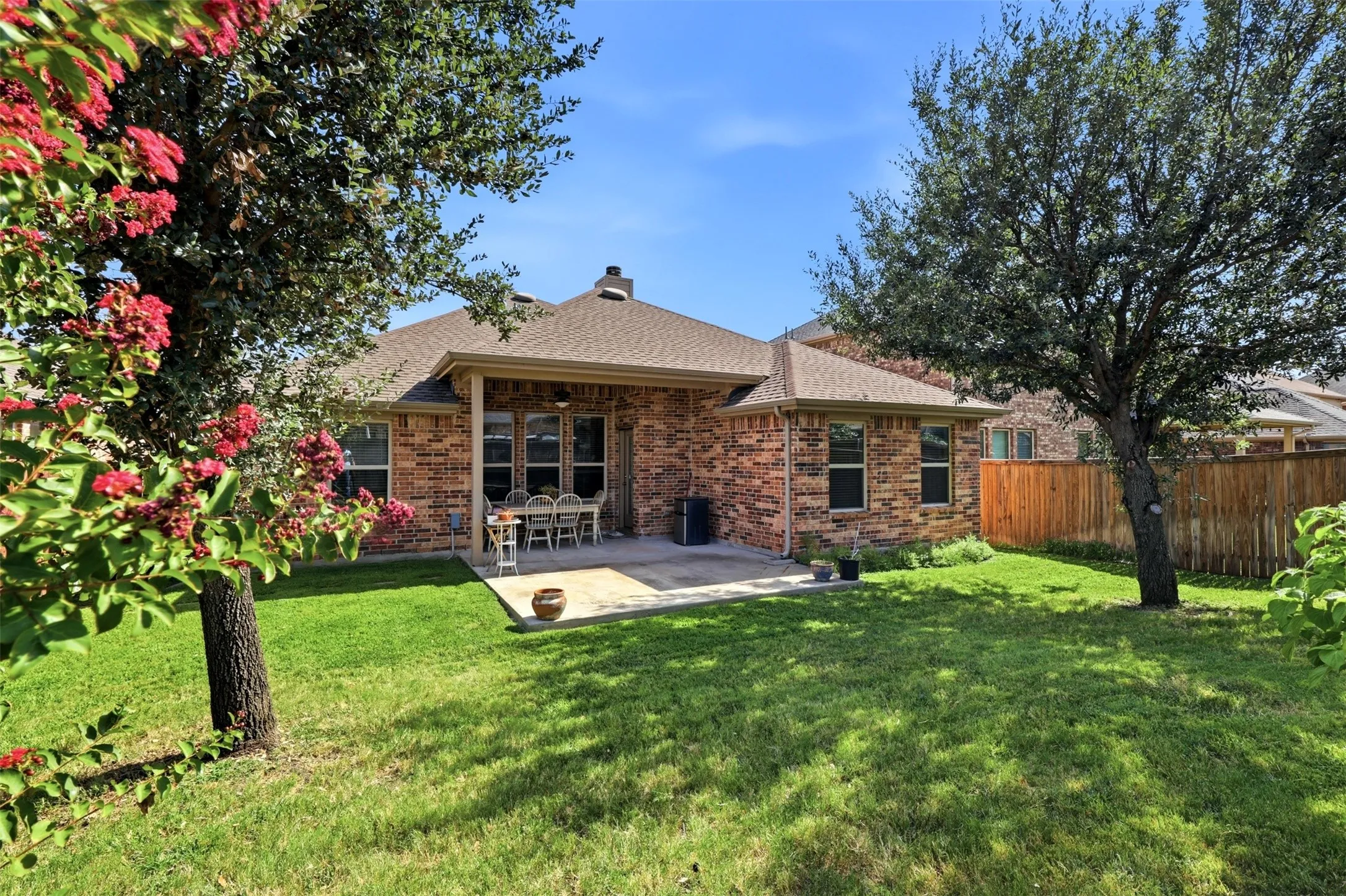 Expansive lawn area with mature trees, a covered patio, and brick exterior