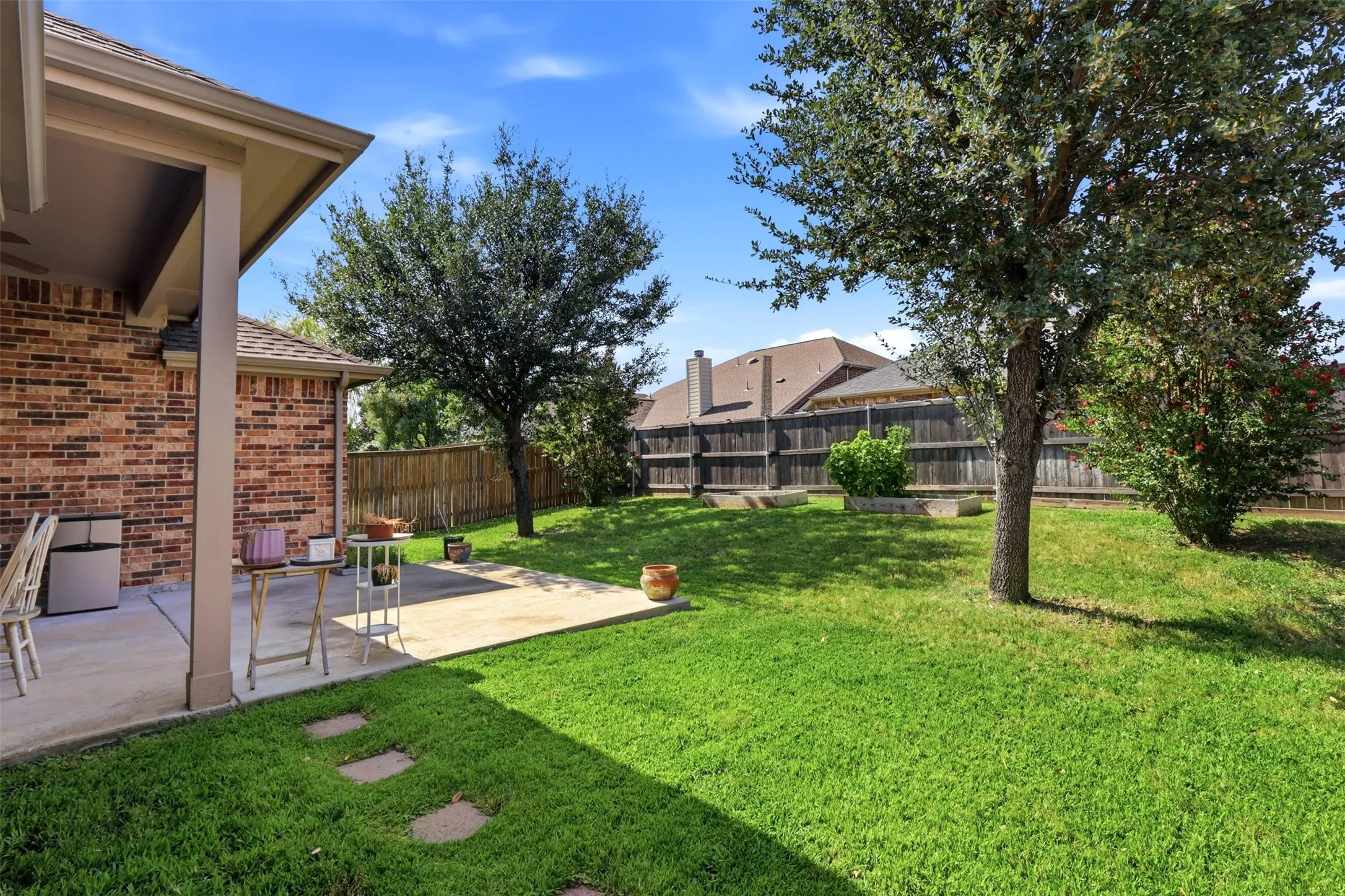 Expansive backyard with a covered patio and concrete slab, featuring mature trees and a wood privacy fence
