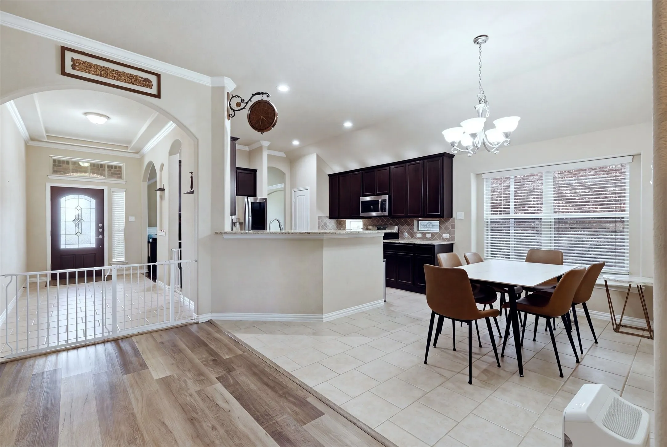 Open concept layout featuring wood-finish flooring, ceramic tile, arched entryway, a built-in breakfast bar, and a chandelier